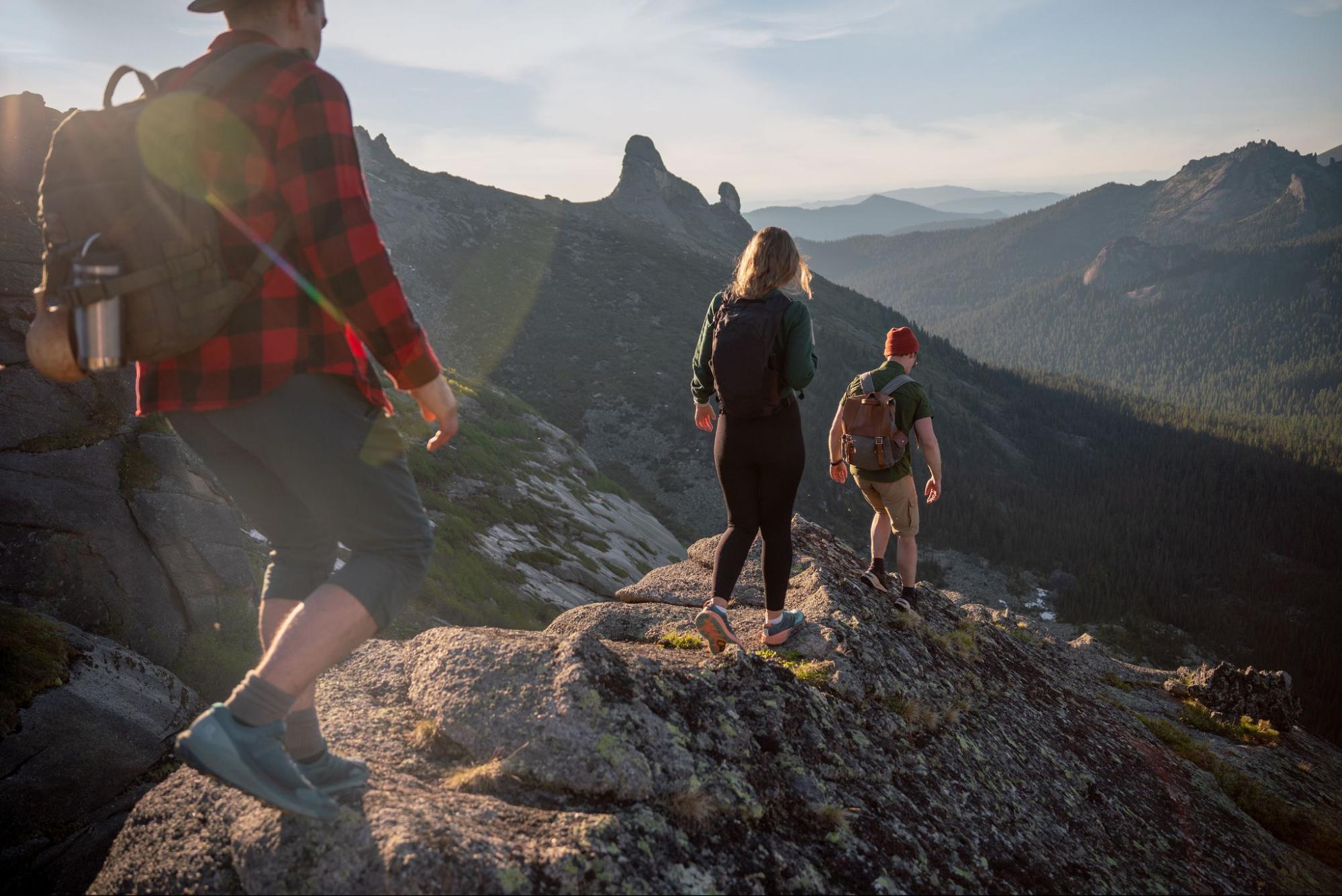Three hikers with backpacks walking along a rocky mountain ridge above forested valleys